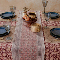 Elegant table setting with a patterned table runner, glasses, and decorative items on a beige background.